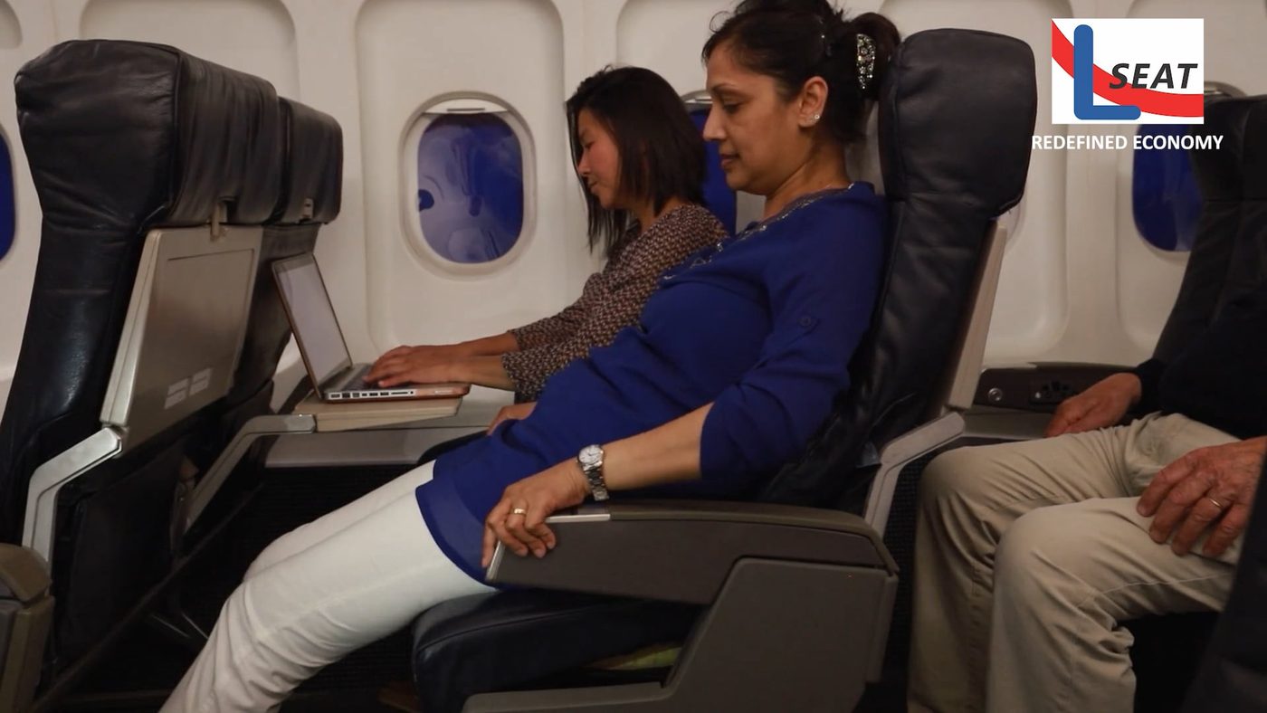 LSEAT economy cabin in service, a passenger working on a laptop at a reclined seat beside the window.