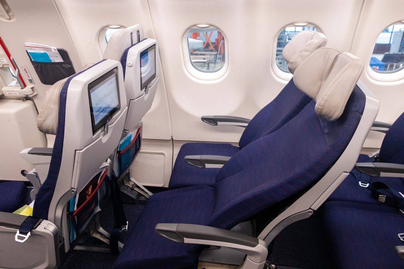Economy cabin with an LSEAT seat in full sleep recline, seat-back inflight entertainment screen in the foreground.