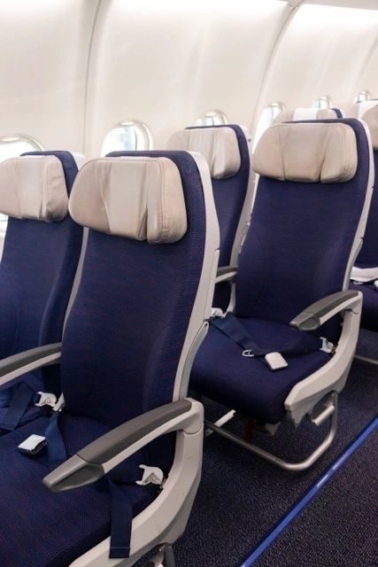 A pair of upright LSEAT economy seats with seat-back inflight entertainment screens and armrests.